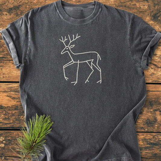 Deer Tribal - Vintage Wash Tee features a minimalist deer drawing on a charcoal-gray shirt, laid on wood. The T-shirt is soft-washed, relaxed fit, showcasing durability and comfort.