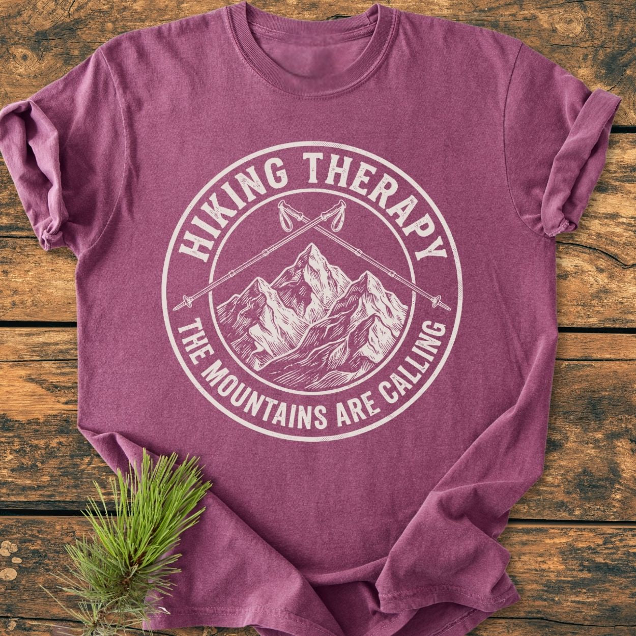 Hiking Therapy - Vintage Wash Tee laid on wood, featuring a mountain emblem with crossed trekking poles and HIKING THERAPY text. Soft-washed, relaxed fit, durable double-needle stitching, pre-shrunk cotton.
