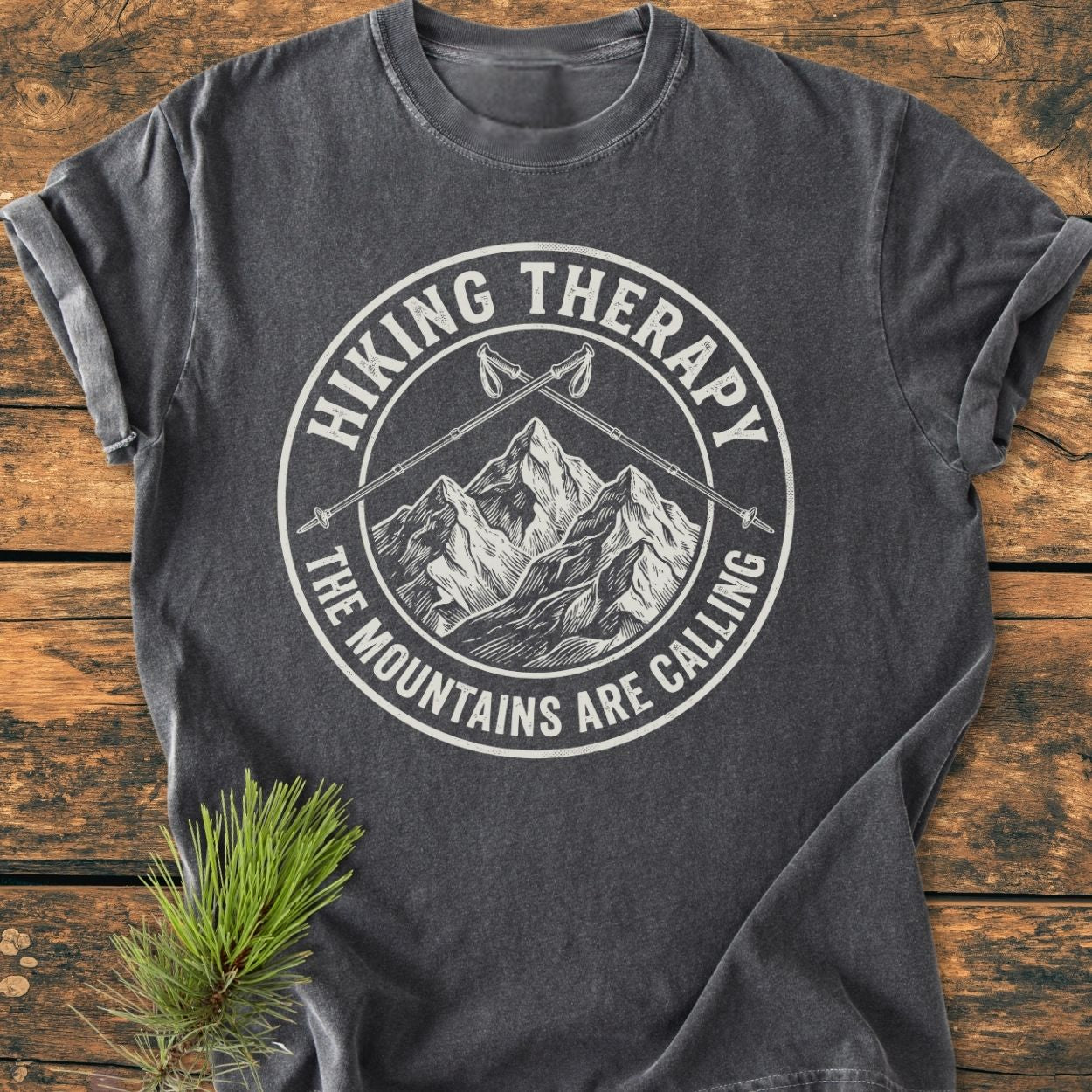 Hiking Therapy - Vintage Wash Tee featuring a circular graphic with mountains and hiking poles, laid flat on wood. Crafted from soft, pre-shrunk, ring-spun cotton for comfort and durability.