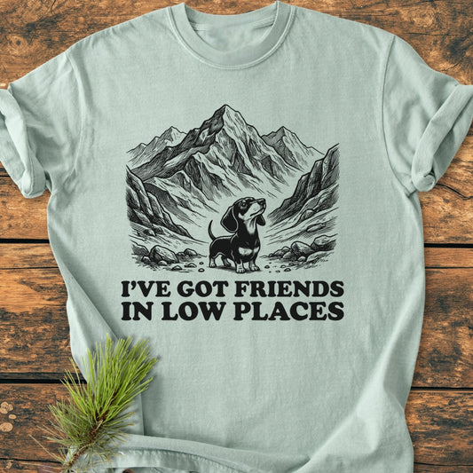 Friends In Low Places - Vintage Wash Tee features a mountainous valley line-drawing with a dachshund and punny caption. Made of soft, durable 100% ring-spun cotton, offering a relaxed fit and garment-dyed comfort.