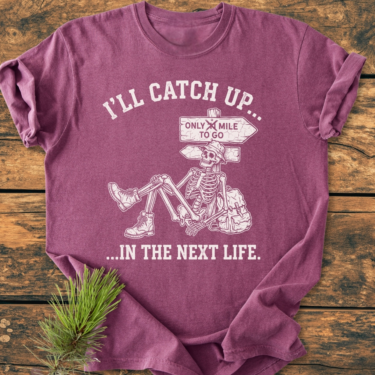 I'll Catch Up - Vintage Wash Tee features a graphic of a skeleton in hiking boots and hat leaning on a trail sign, emphasizing its relaxed fit and garment-dyed, soft-washed fabric.