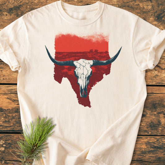 Hike Texas - Vintage Wash Tee featuring a longhorn skull graphic on a cream T-shirt, displayed on a wooden surface with a pine sprig accent, highlighting its relaxed, durable design.