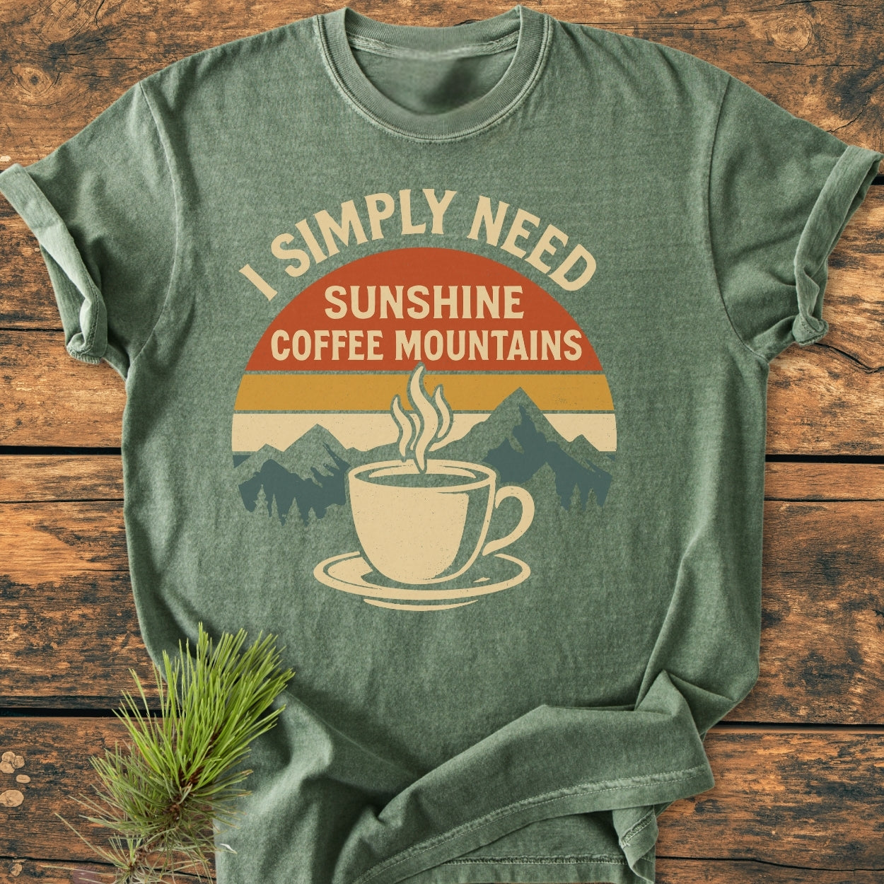 Retro Sunrise Coffee & Mountains - Vintage Wash Tee on wooden surface, featuring a steaming coffee cup graphic with mountains and sunset, heather-green, soft-washed, relaxed fit, 100% ring-spun cotton, durable stitching.