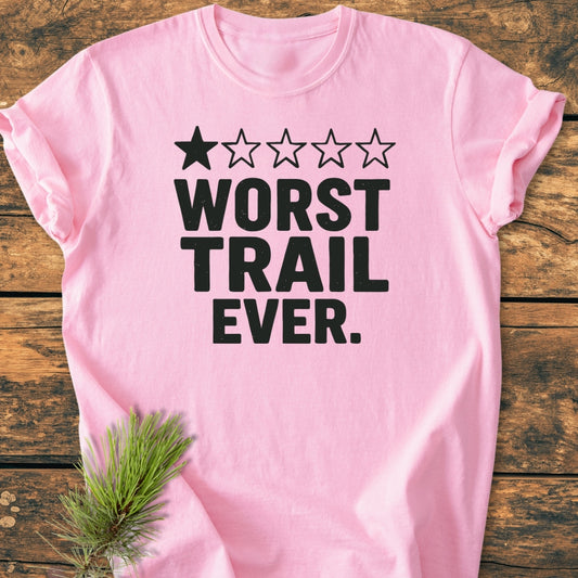 Light-pink Worst Trail Ever - Vintage Wash Tee with a black one-star graphic and bold text, laid on wood. A pine sprig peeks from under, showcasing its cozy, durable design.