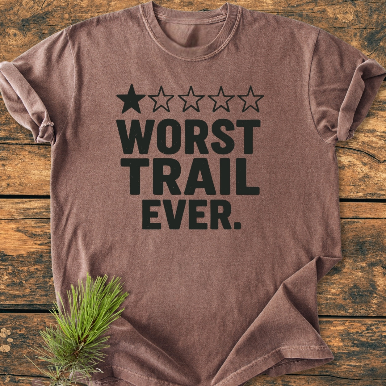 Worst Trail Ever - Vintage Wash Tee features bold black text and a one-star rating, laid flat on wood. Crafted from 100% ring-spun cotton, the tee offers a relaxed, cozy fit.