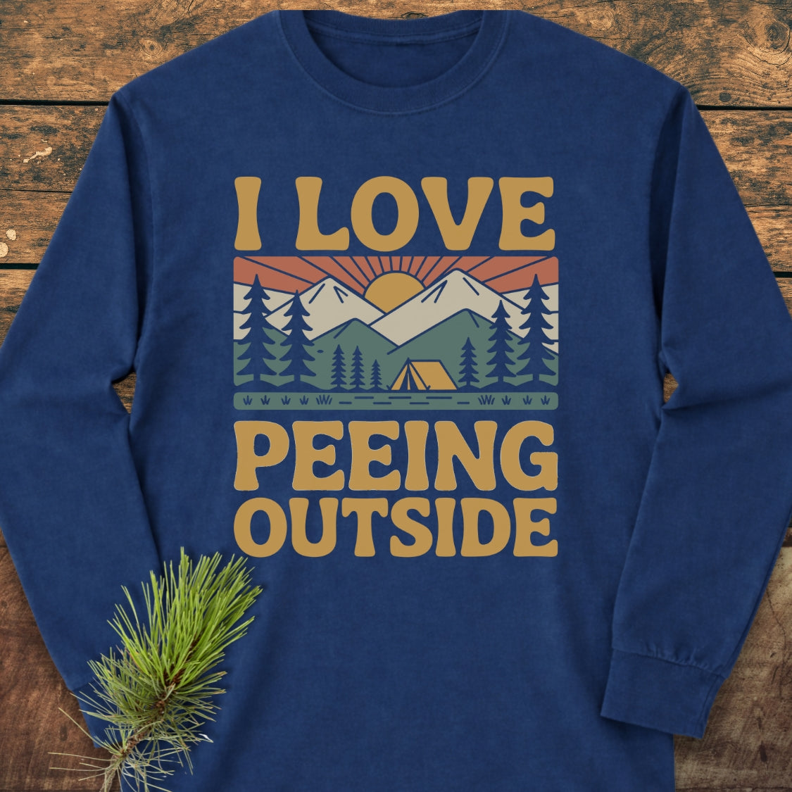 Navy-blue I Love Peeing Outside long-sleeve tee featuring a playful outdoor scene with pine trees, a tent, river, mountains, and sun. Made from 100% ring-spun cotton, offering a relaxed fit.