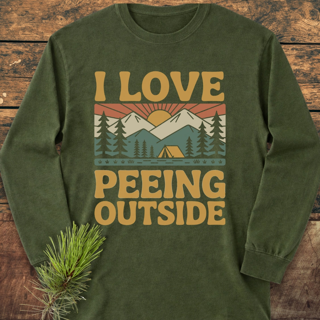Forest-green I Love Peeing Outside long-sleeve tee featuring a retro nature scene with mountains, pine trees, and a tent; styled with a pine sprig accent, offering a soft, relaxed fit.