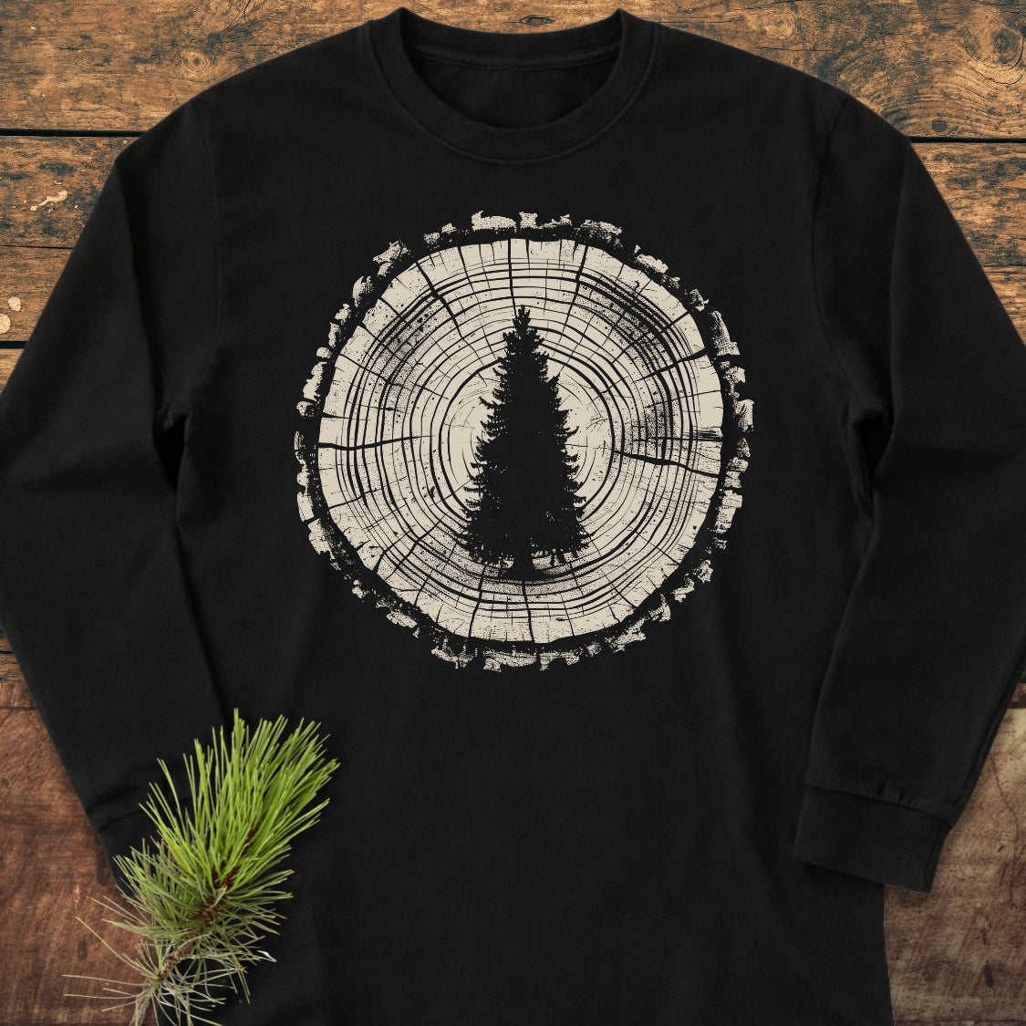 Rooted In The Wild Long-Sleeve Tee featuring a large tree-cross-section with a pine tree silhouette. Laid on wood, it embodies nature's essence, crafted from 100% ring-spun cotton for comfort and style.