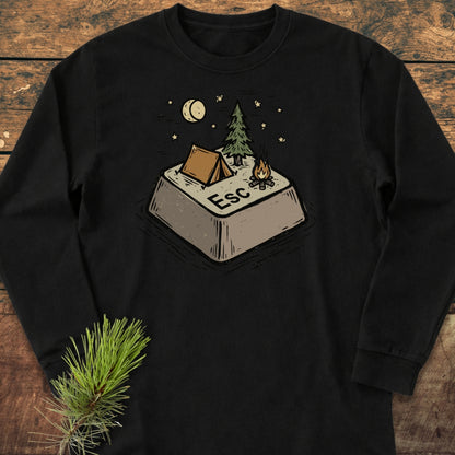 Escape Long-Sleeve Tee featuring a giant Esc key illustration transformed into a campsite with a tent, pine tree, campfire, and starry night, laid on a wooden surface with a pine sprig.