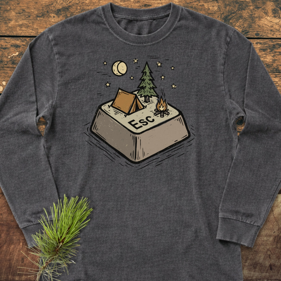 Escape Long-Sleeve Tee featuring a cozy camping graphic on a dark-gray shirt. Displayed on wood, it highlights a relaxed fit, ideal for casual comfort with a camping-inspired design.