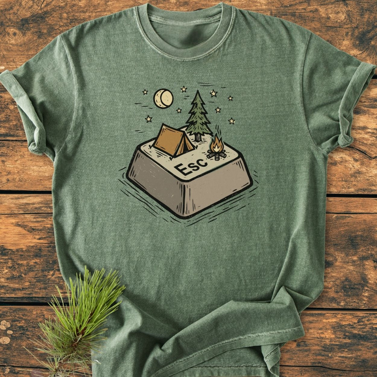 Escape - Vintage Wash Tee features an olive-green T-shirt with a graphic of a campsite on a keyboard Esc key, highlighting a tent, pine tree, campfire, and night sky.