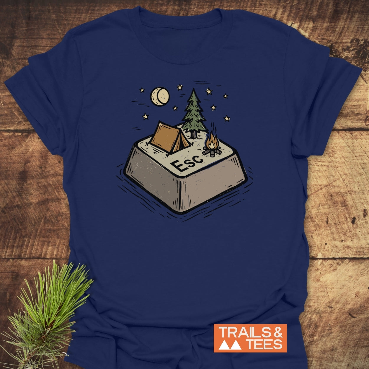 Escape T-Shirt featuring a whimsical “Esc” key campsite illustration with a tent, tree, campfire, moon, and stars. Includes “TRAILS & TEES.” logo, crafted for comfort and adventure.