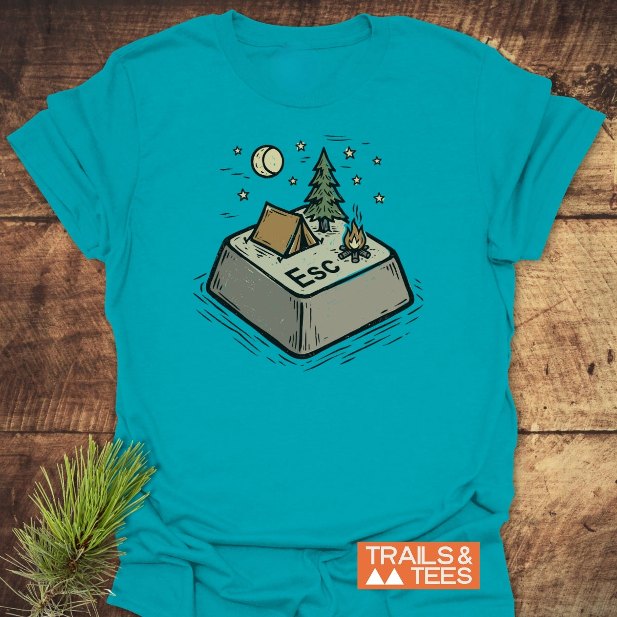Escape T-Shirt features a playful graphic of a Esc key turned camping scene with tent, pine tree, and campfire, set against a teal backdrop, branded by TRAILS & TEES.