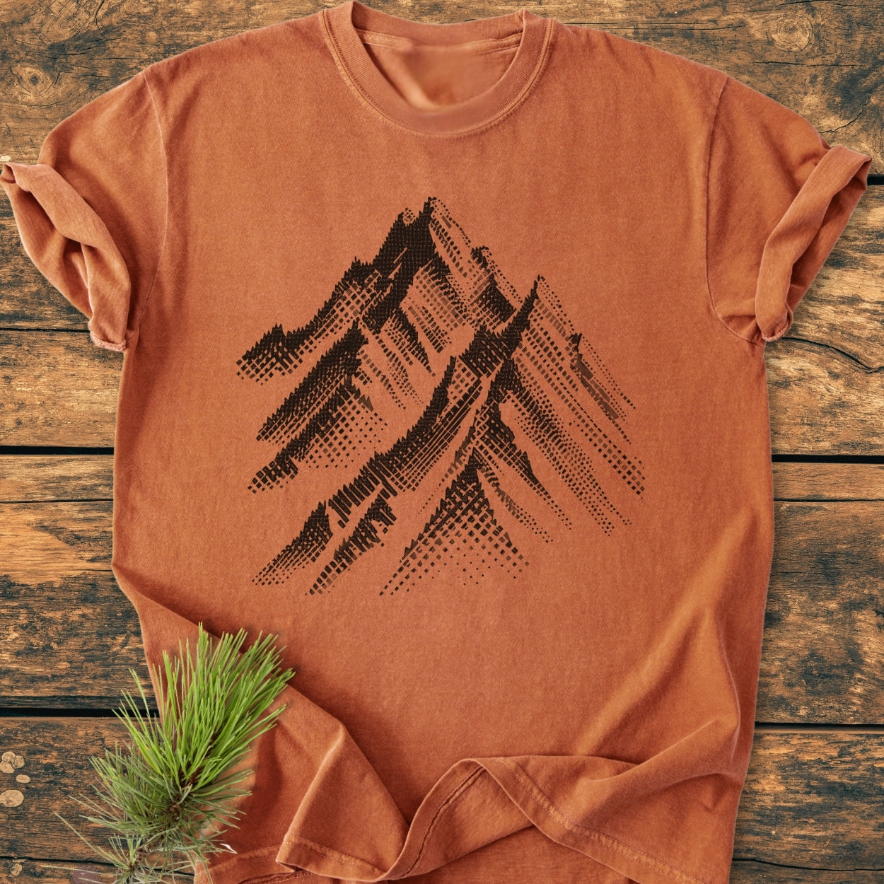 Take Me Higher - Vintage Wash Tee: A rust-orange, short-sleeved T-shirt with a black halftone mountain design on the chest, laid on wood. Features durable stitching and a relaxed fit for daily comfort.