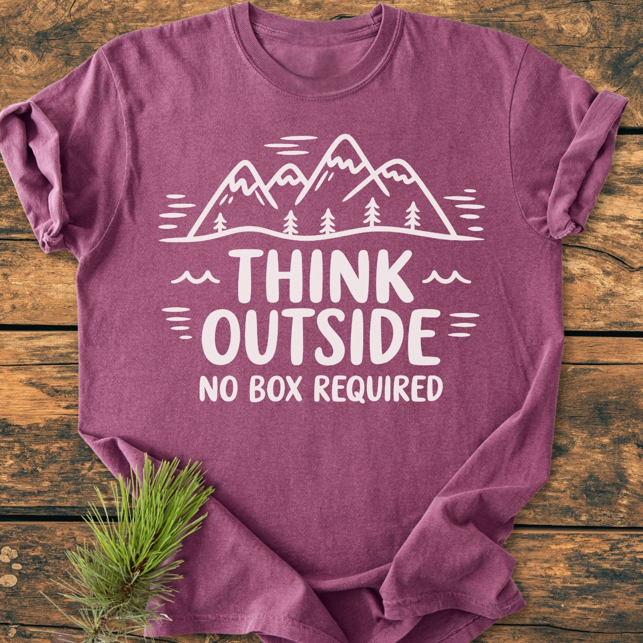 Think Outside - Vintage Wash Tee featuring a white line-art mountains and trees design with slogan on a mauve-purple backdrop, laid flat on wood. Cozy, relaxed fit, 100% ring-spun cotton.