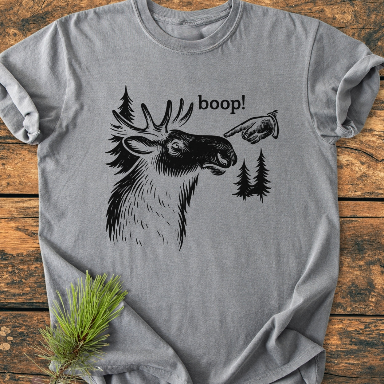 BOOP Moose Funny - Vintage Wash Tee features a heather-gray design with a moose head, hand, and boop! text. Laid on wood, highlighting its soft, relaxed fit, and durable stitching.