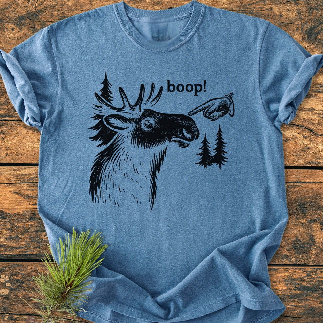 BOOP Moose Funny - Vintage Wash Tee features a moose illustration with boop! text and vintage hand design on a light-blue, soft-washed t-shirt. Fir-tree silhouettes and pine needles accentuate the design.