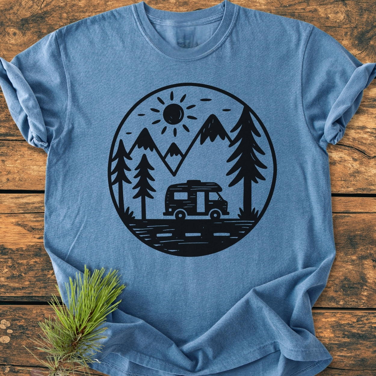 Freedom Is Found Outside - Vintage Wash Tee featuring a camper van graphic with pine trees and mountains, laid on wood with a pine sprig. Heather-blue, relaxed fit, showcasing cozy, durable craftsmanship.