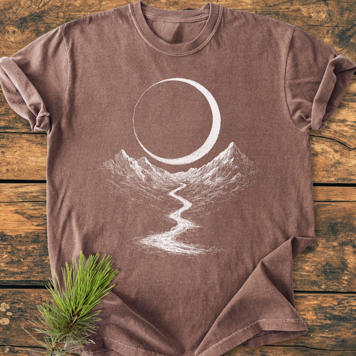 Eclipse Trail - Vintage Wash Tee features a minimalist landscape of a crescent over mountain peaks and a river, printed on a washed-brown crew-neck T-shirt with a cozy, relaxed fit.