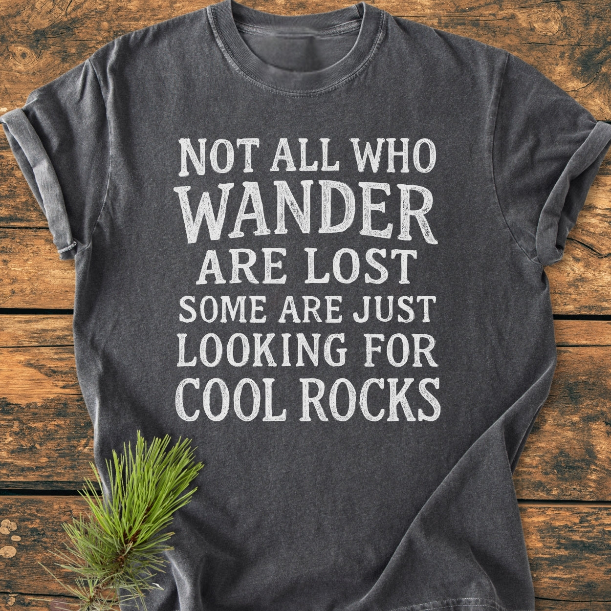 Dark-gray Not All Who Wander Are Lost Rustic Chalkboard - Vintage Wash Tee with white distressed lettering, laid flat on wood, showcasing its soft-washed garment-dyed fabric and relaxed fit.