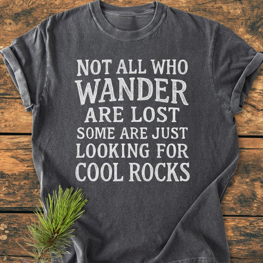 Dark-gray Not All Who Wander Are Lost Rustic Chalkboard - Vintage Wash Tee with white distressed lettering, laid flat on wood, showcasing its soft-washed garment-dyed fabric and relaxed fit.