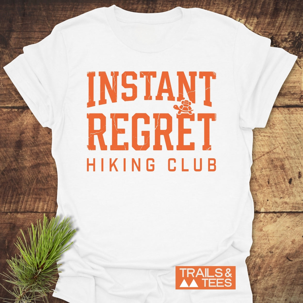 The Instant Regret Hiking Club T-Shirt features a rustic design with INSTANT REGRET in orange letters and a turtle icon, perfect for outdoor enthusiasts seeking comfort and style.