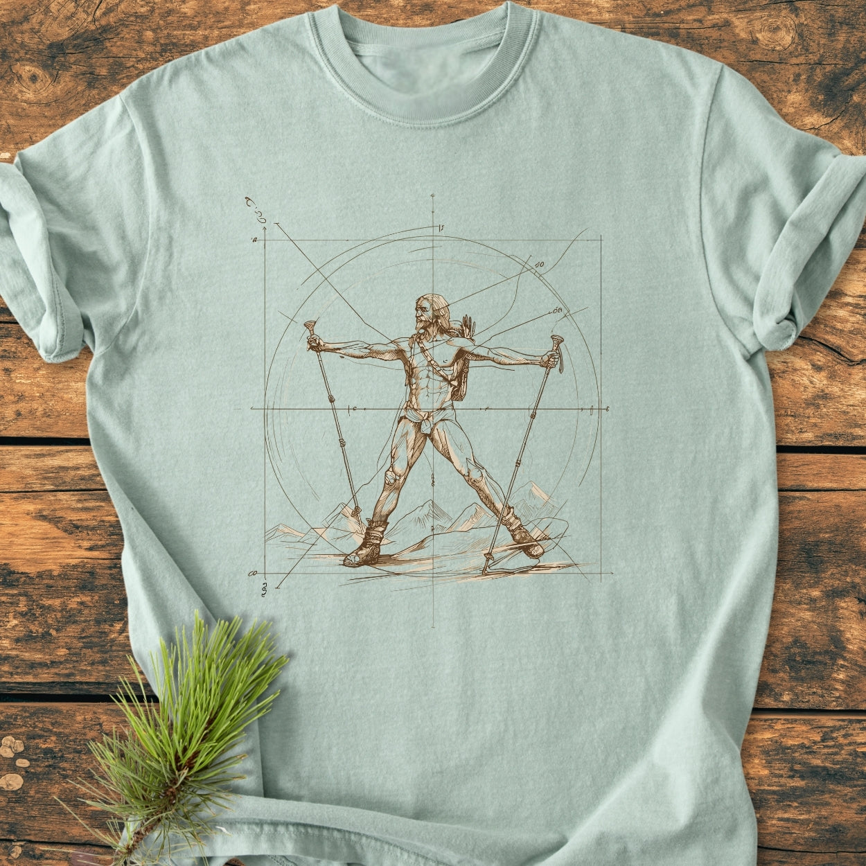 Vitruvian Hiker - Vintage Wash Tee features a Da Vinci-inspired skier graphic, laid flat on wood, with pine sprig. Made of soft, durable, garment-dyed 100% ring-spun cotton for relaxed comfort.