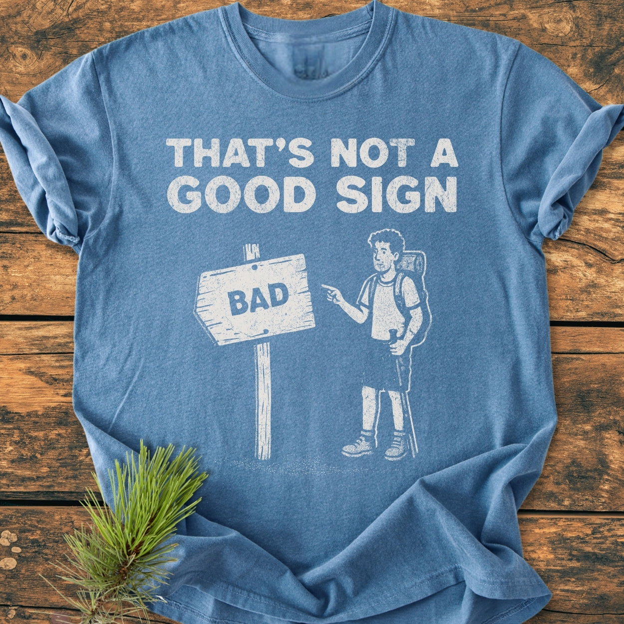 Bad Sign - Vintage Wash Tee features a cartoon hiker pointing at a signpost with BAD on a soft, relaxed fit, blue shirt, highlighting its durable, garment-dyed, 100% ring-spun cotton fabric.
