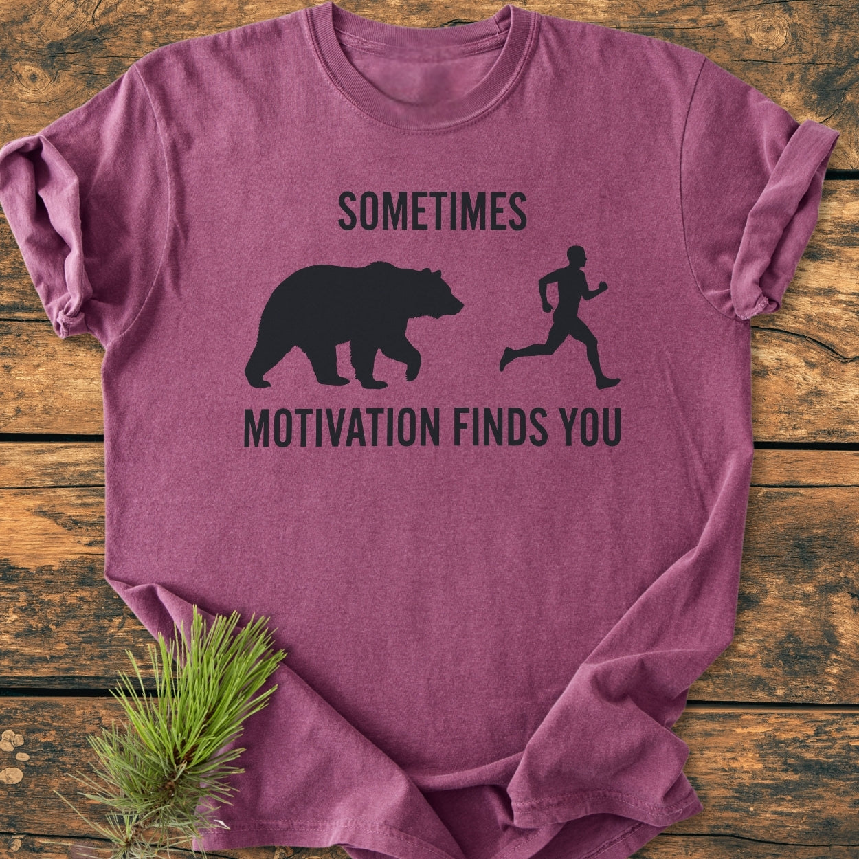 Sometimes Motivation Finds You - Vintage Wash Tee showing a humorous bear-chase design on a heather-purple T-shirt, laid on wood with a pine sprig, highlighting its soft, relaxed fit.