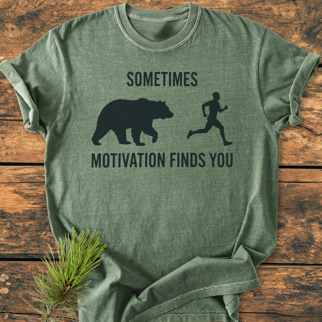 Sometimes Motivation Finds You - Vintage Wash Tee displayed flat, forest-green, with a bear and human graphic, rustic pine sprig beside, emphasizing comfort and durability with garment-dyed, ring-spun cotton.