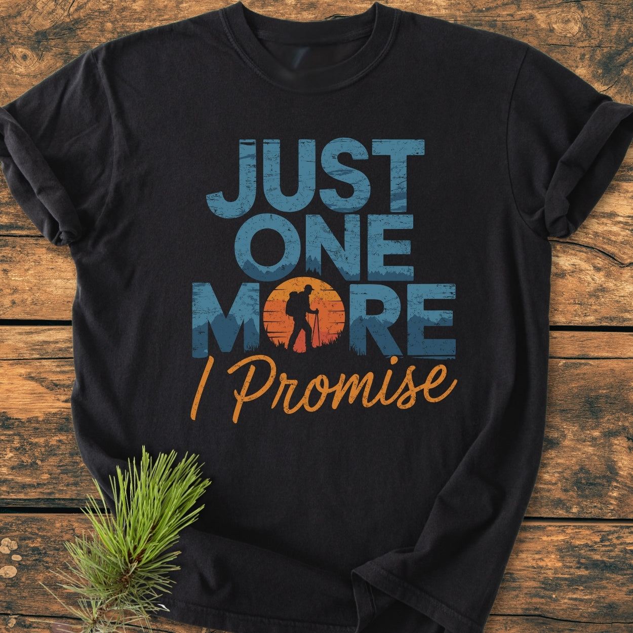 Just One More I Promise - Vintage Wash Tee: Black T-shirt with “JUST ONE MORE” and hiker silhouette design. Laid on wood, featuring a relaxed fit and soft-washed, garment-dyed fabric for comfort.