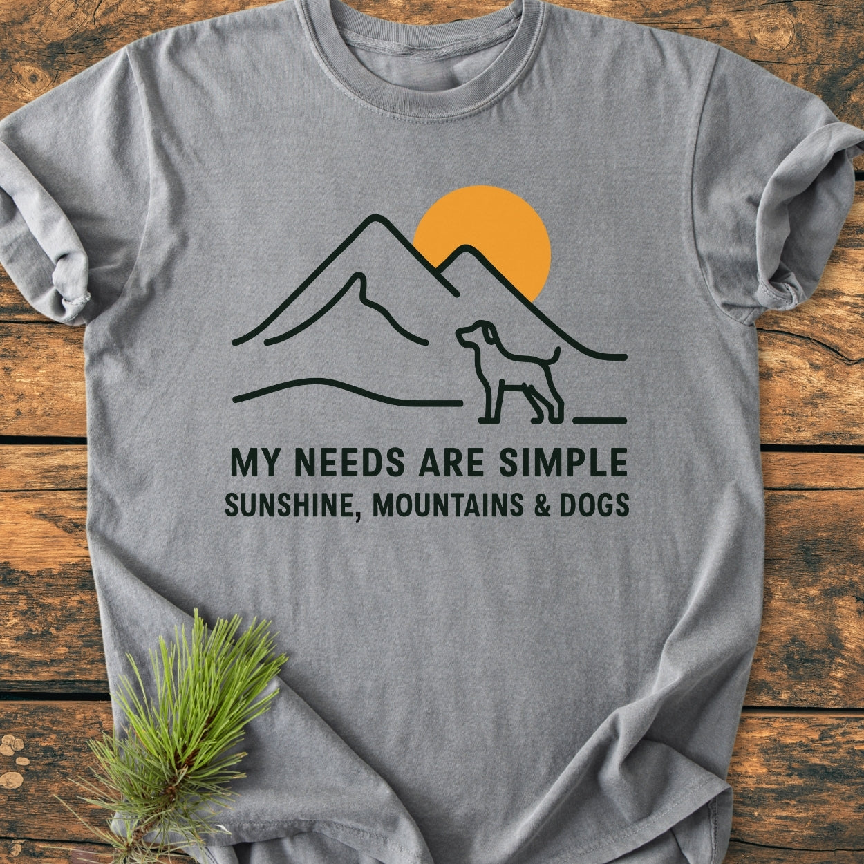 Simple Joys Mountains - Vintage Wash Tee features a minimalist mountain and dog design with the slogan MY NEEDS ARE SIMPLE SUNSHINE, MOUNTAINS & DOGS. Laid flat, it exhibits a cozy, relaxed fit.