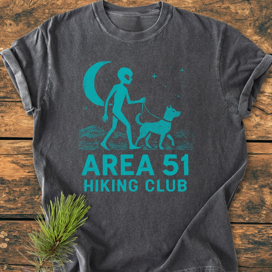 Area 51 Hiking Club - Vintage Wash Tee featuring a stylized alien walking a dog under a crescent moon, laid on wood. Made from 100% ring-spun cotton, offering comfort and durability.
