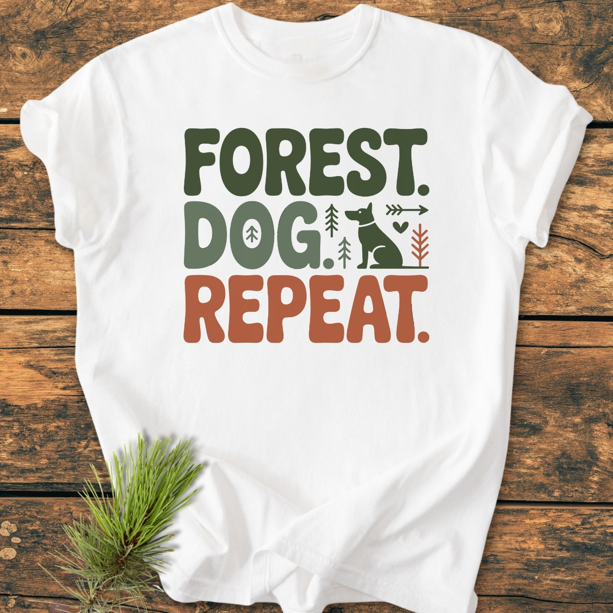 Forest Dog Repeat - Vintage Wash Tee displayed on a wooden surface, features a graphic with “FOREST. DOG. REPEAT.” in green and brown, accompanied by icons of a dog, trees, and a heart.