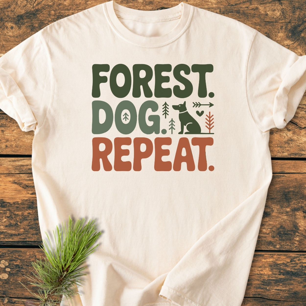 Forest Dog Repeat - Vintage Wash Tee on wooden surface, featuring bold earthy text and simple graphics of a dog, trees, heart, and arrow. Cream-colored, soft-washed, relaxed fit, durable with double-needle stitching.