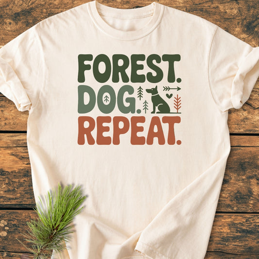 Forest Dog Repeat - Vintage Wash Tee on wooden surface, featuring bold earthy text and simple graphics of a dog, trees, heart, and arrow. Cream-colored, soft-washed, relaxed fit, durable with double-needle stitching.