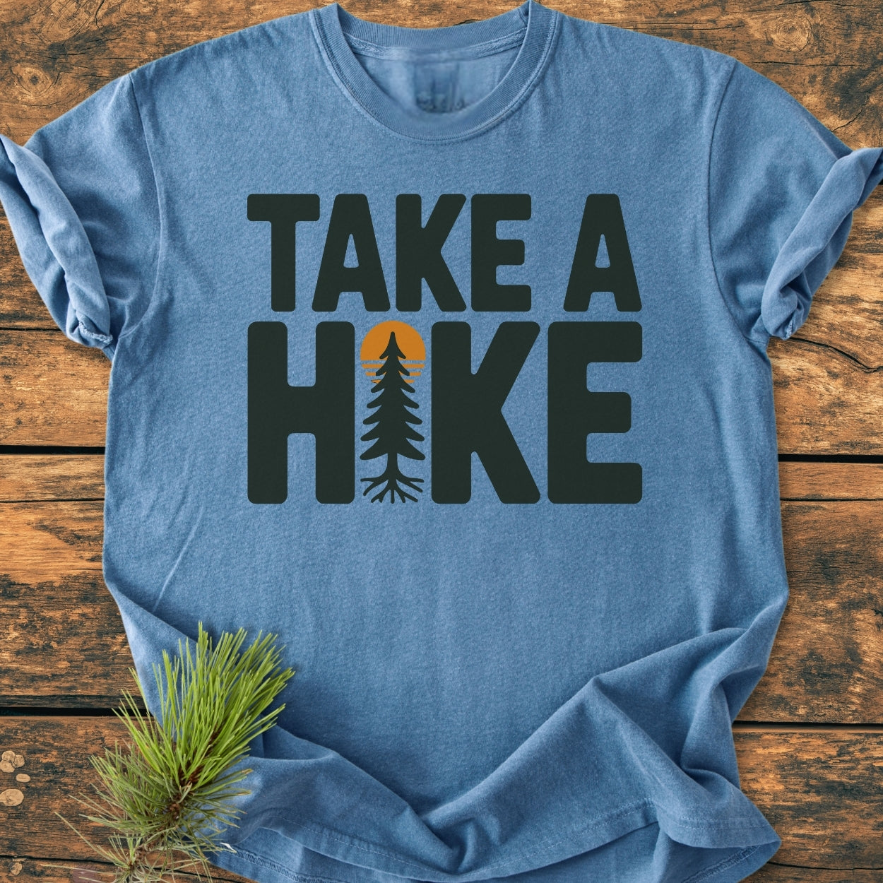 Take A Hike - Vintage Wash Tee features a bold TAKE A HIKE graphic with a tree motif, laid on rustic wood. The heather-blue tee embodies comfort with its relaxed fit and durable, soft-washed cotton.