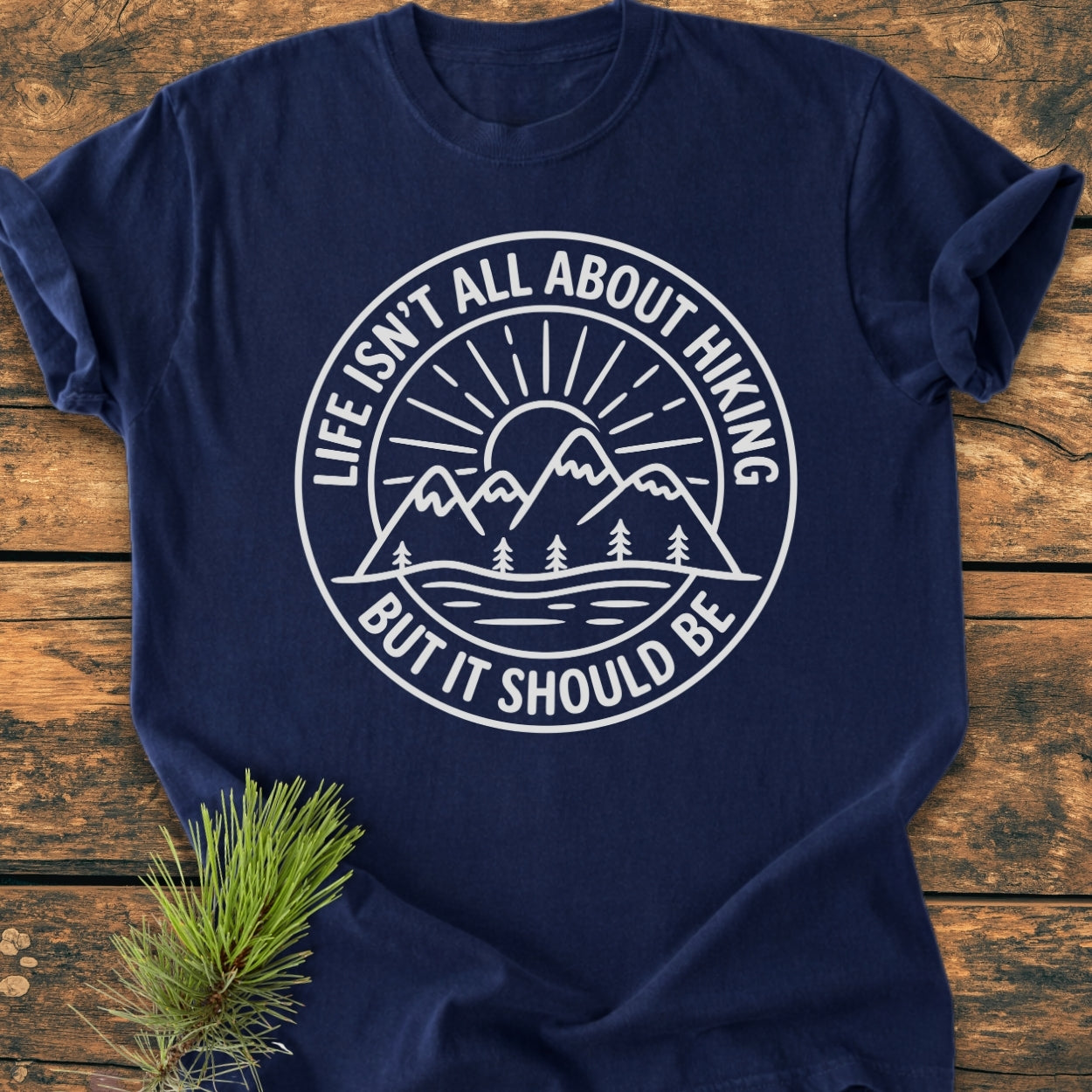 Life Isn't All About Hiking - Vintage Wash Tee features a circular graphic of mountains and a sunrise, emphasizing adventure. Laid on wood, the tee showcases a cozy, relaxed fit.