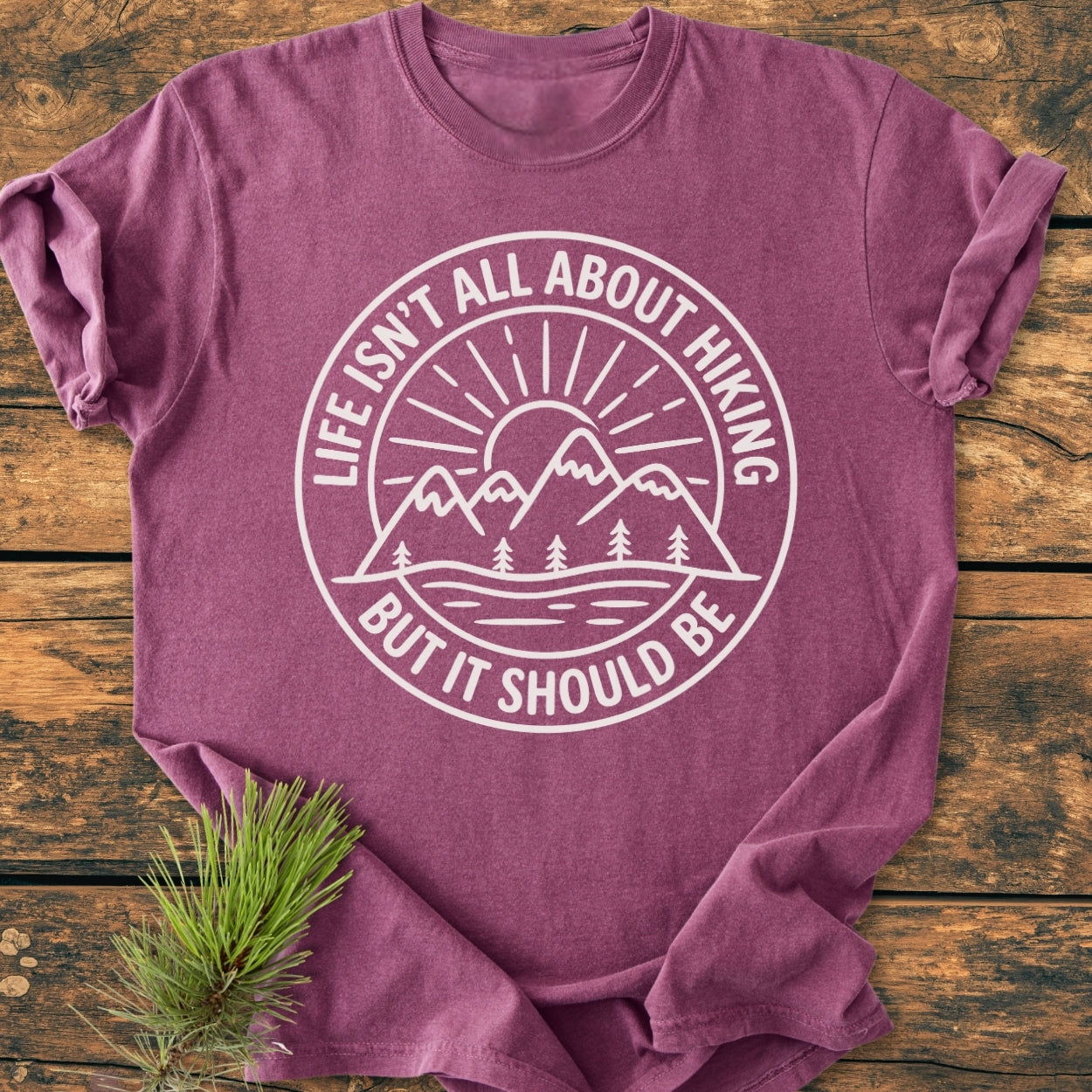 Life Isn't All About Hiking - Vintage Wash Tee: Purple-heather T-shirt with a white mountain and sun graphic, slogan encircling it; laid on wood, pine sprig beside, epitomizing outdoor adventure spirit.