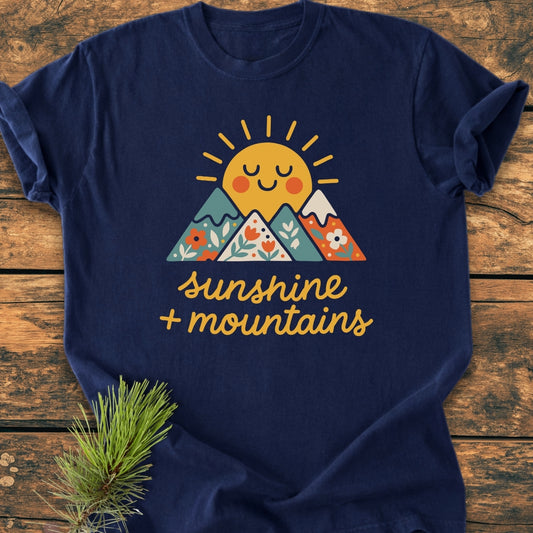 Sunshine And Mountains - Vintage Wash Tee features a smiling sun graphic over floral-patterned mountains on a navy-blue Comfort Colors T-shirt, offering a cozy, relaxed fit with durable double-needle stitching.