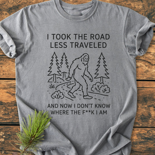 I Took The Road Less Traveled - Vintage Wash Tee features Bigfoot on a forest trail with humorous text. Gray, relaxed fit, 100% cotton, perfect for daily comfort and style.