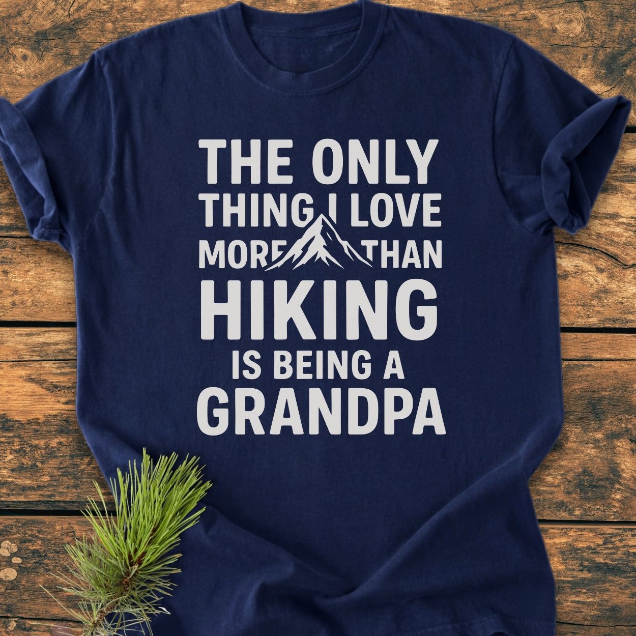Hiking Grandpa - Vintage Wash Tee featuring a mountain graphic and playful text, displayed on wood with a pine sprig, showcasing its cozy, relaxed fit and durable, soft-washed fabric.