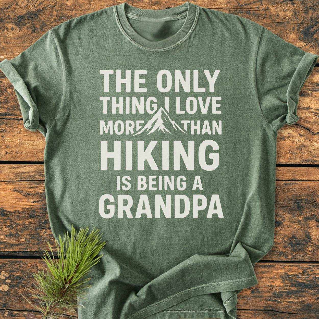 Forest-green Hiking Grandpa - Vintage Wash Tee with white text and mountain graphic, laid flat on wood. Features durable, soft-washed, pre-shrunk cotton, relaxed fit, double-needle stitching, and tubular shape.