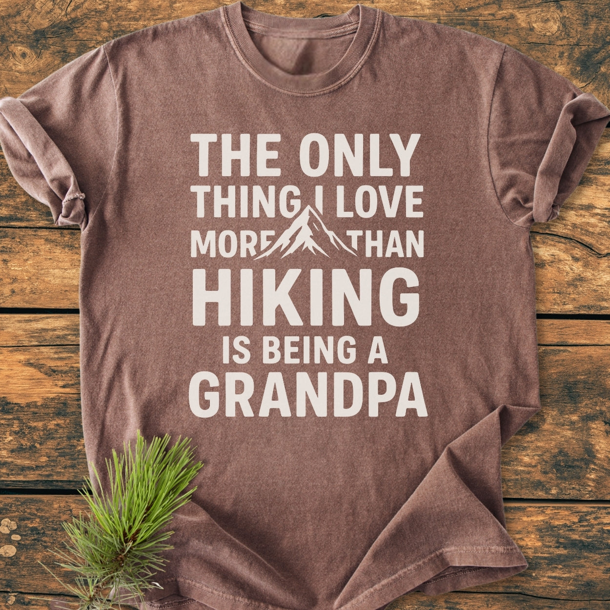 Hiking Grandpa - Vintage Wash Tee: Brown short-sleeve T-shirt with THE ONLY THING I LOVE MORE THAN HIKING IS BEING A GRANDPA slogan and mountain graphic, laid flat on wooden surface.