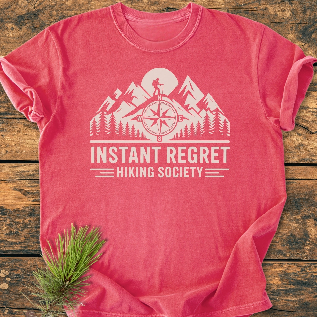 Instant Regret Hiking Society - Vintage Wash Tee features a mountain scene with a hiker, pine trees, and compass, humorously highlighting outdoor adventures. Made from soft-washed, durable 100% ring-spun cotton.