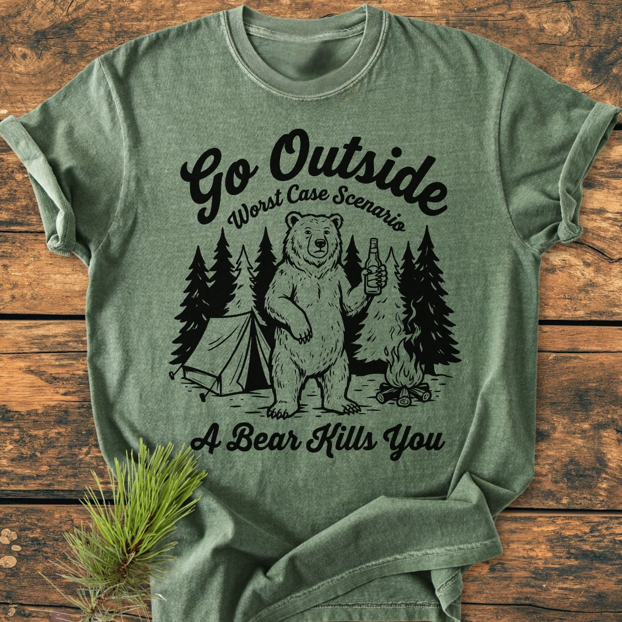 Go Outside - Vintage Wash Tee featuring a cartoon bear with a beer, camping scene, and humorous slogan, laid on wood with pine sprig; relaxed fit, durable, 100% ring-spun cotton.