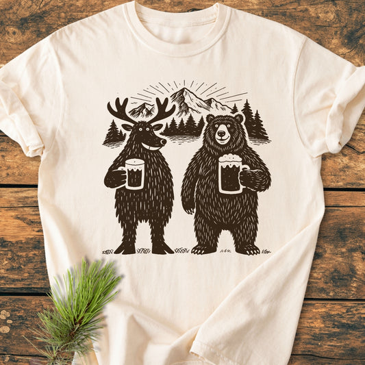 Bear, Deer And Beer - Vintage Wash Tee features playful moose and bear with beer mugs, set against pine trees and mountain backdrop, enhancing its rustic charm on soft, relaxed-fit, cream-colored fabric.