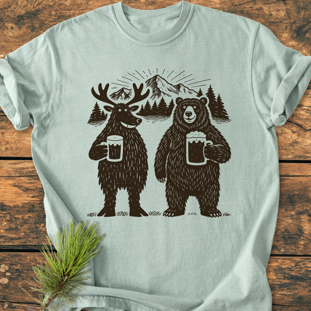 Bear, Deer And Beer - Vintage Wash Tee features a cartoon moose and bear with beer mugs on light-green fabric, styled with a pine sprig, highlighting its relaxed fit and durable stitching.