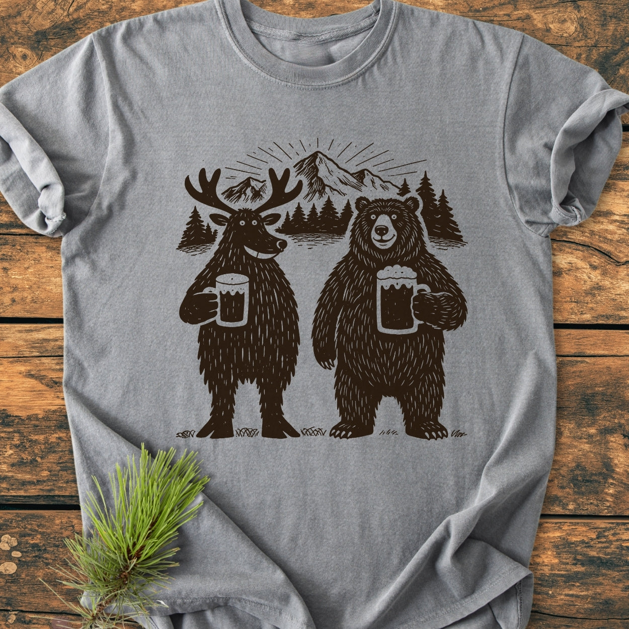 Bear, Deer And Beer - Vintage Wash Tee: Heather-gray T-shirt with moose and bear illustration holding beer mugs, laid on rustic wood with a pine branch. Cozy, relaxed fit, garment-dyed for softness.