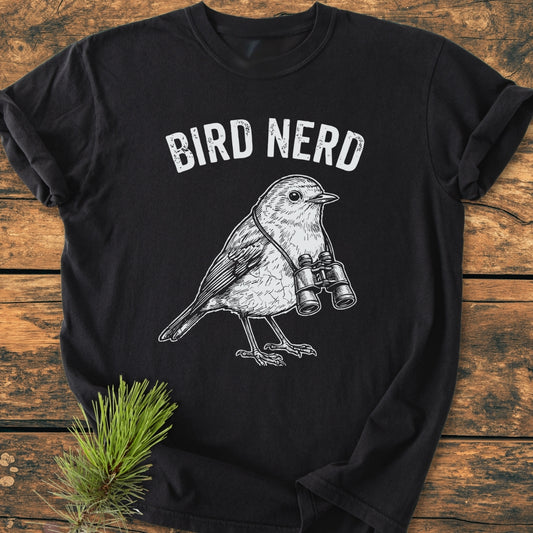 Bird Nerd - Vintage Wash Tee features BIRD NERD text and a songbird with binoculars on soft black fabric, styled with a pine sprig on a wooden surface.